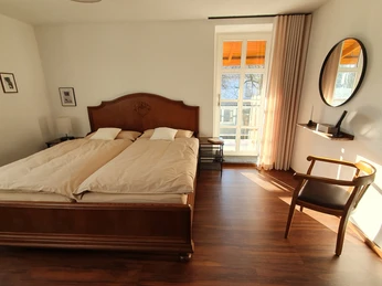 Gästezimmer anna und Hieni (1).jpg Helles Gästezimmer mit einem Kingsize-Holzbett, schlichter Dekoration und einem Fenster mit Blick ins Freie.