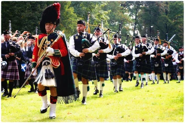 Highland Games Einmarsch Eine Gruppe von Männern in Kilts marschiert mit Dudelsäcken über eine Wiese.