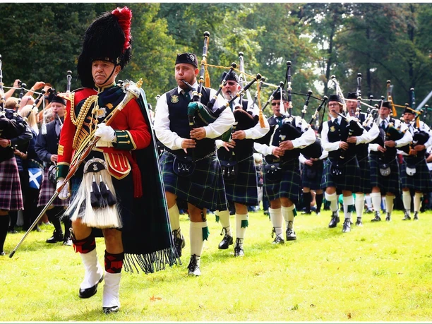 Highland Games Einmarsch Eine Gruppe von Männern in Kilts marschiert mit Dudelsäcken über eine Wiese.