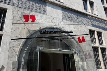 Eingangstür mit rundem Bogen, über der ein gläsernes Schild mit dem Aufdruck "Internationales Zeitungsmuseum" befestigt ist.