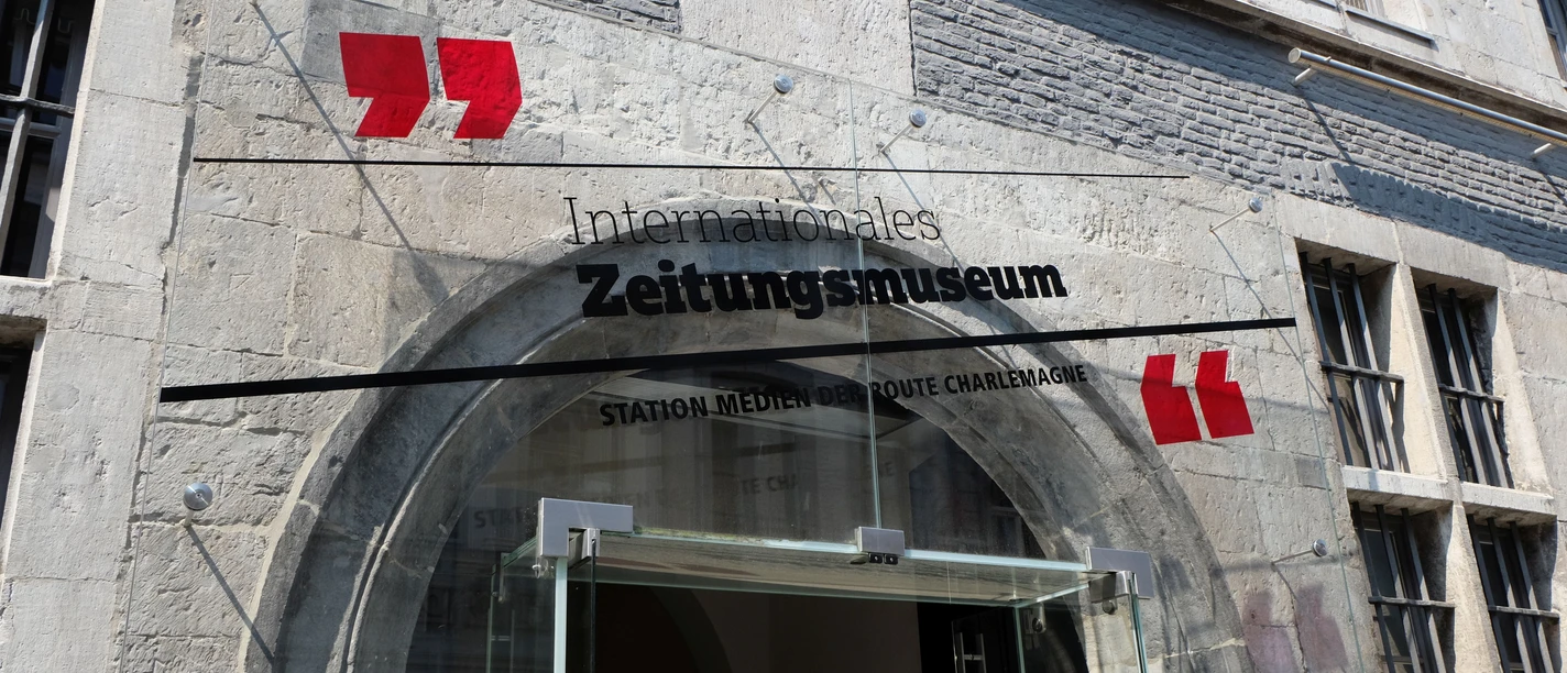 Eingangstür mit rundem Bogen, über der ein gläsernes Schild mit dem Aufdruck "Internationales Zeitungsmuseum" befestigt ist.