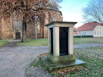 Ein steinernes Monument gewidmet einem Bischof vor der Kulisse einer historischen Backsteinkirche.