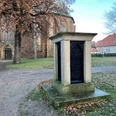 Ein steinernes Monument gewidmet einem Bischof vor der Kulisse einer historischen Backsteinkirche.