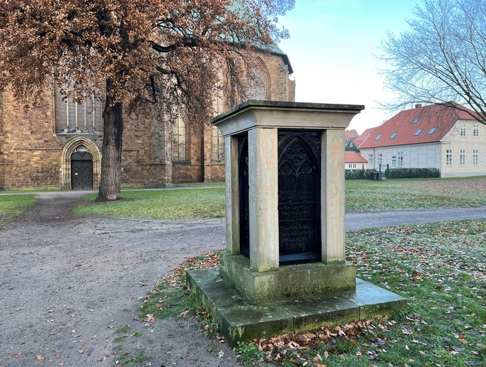 Bischofsdenkmal Verden Ein steinernes Monument gewidmet einem Bischof vor der Kulisse einer historischen Backsteinkirche.