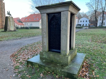 Bischofsdenkmal Verden Steinernes Denkmal mit filigran gearbeiteter Inschrift, umgeben von herbstlichem Laub im Park.