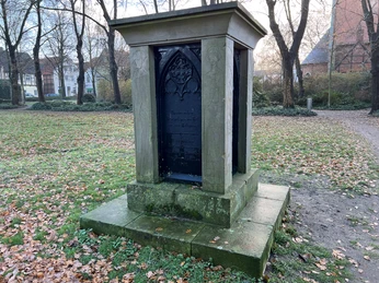 Historisches Denkmal aus Stein mit Reliefs, umgeben von herbstlichem Laub auf einem Rasenplatz.