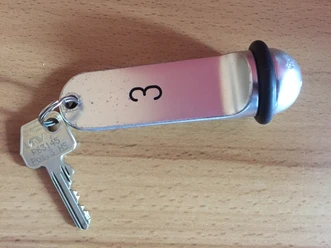 Een metalen sleutelhanger met het cijfer 3 en een sleutel op een houten oppervlak.