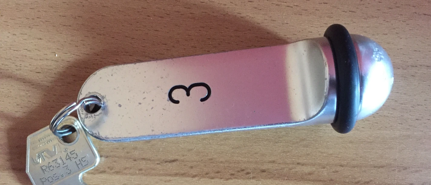 A metal key ring with the number 3 and an attached key on a wooden surface.