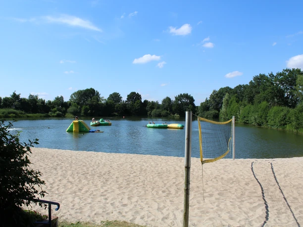 Naturfreibad Eystrup Sandstrand mit Volleyballnetz am Naturfreibad Eystrup. Im Wasser sind aufblasbare Spielgeräte.