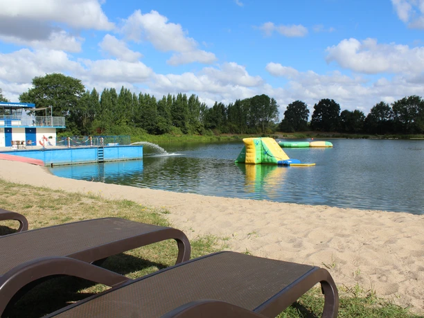 Naturfreibad Eystrup (Eigenname) Sandstrand mit Volleyballnetz, Schwimmbereich und Wasserspielgerät am Freibad Eystrup.
