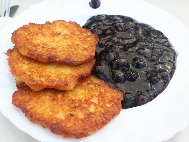 Bickbeernhof Drie goudbruine aardappelpannenkoekjes naast een portie sappige bosbessencompote op een wit bord.