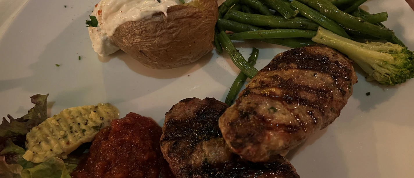 A plate of grilled mince steaks, green beans, broccoli florets and baked potato with sour cream.