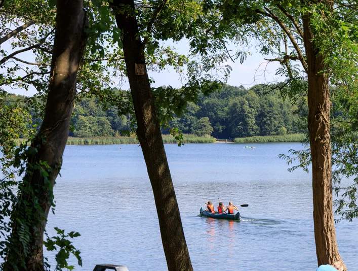 Sommerliche Idylle am Kronensee in Ostercappeln Kanu mit drei Personen auf ruhigem See, umgeben von dichten Bäumen und grünem Ufer.