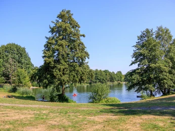 Ausflugsziel Kronensee im Osnabrücker Land Grüner Park mit See, umgeben von Bäumen, zwei Personen paddeln auf dem Wasser.