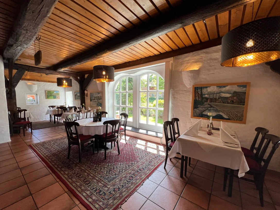 Helles Restaurant mit Holzbalkendecke, großen Fenstern, Teppich und liebevoll gedeckten Tischen.