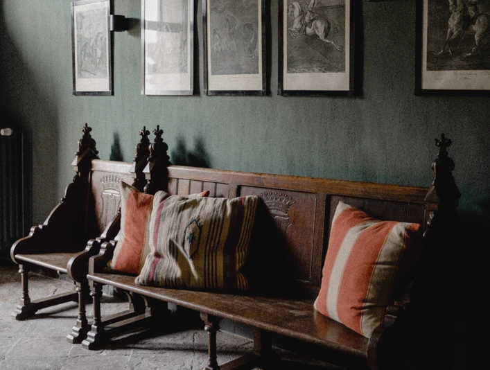 RDF_MG_4961.jpg Holzbank mit dekorativen Kissen vor einer dunklen Wand, geschmückt mit gerahmten Schwarz-Weiß-Bildern.