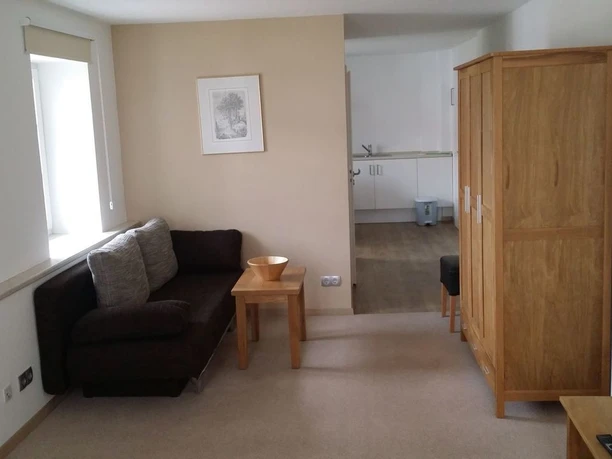 Blick in Wohnzimmer und Küche Offene Wohnküche mit moderner Einrichtung, Holzschränken, Sofa und hellen Wänden.