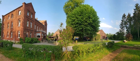 001-Gut-Externbrock_web.jpg Historisches Backsteingebäude mit grüner Hecke und großen Bäumen, ländliche Umgebung.