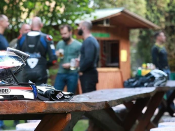 002Gut-Externbrock_web.jpg Motorradfahrer genießen gesellige Stunden neben Holztischen im Grünen, Helme liegen auf den Tischen.