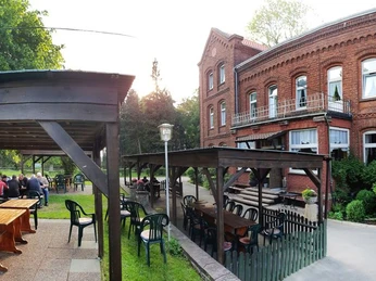 004-Gut-Externbrock-Aussenanlage_web.jpg Historische Backsteinfassade eines Gebäudes mit angrenzender überdachter Terrasse und Sitzmöglichkeiten.