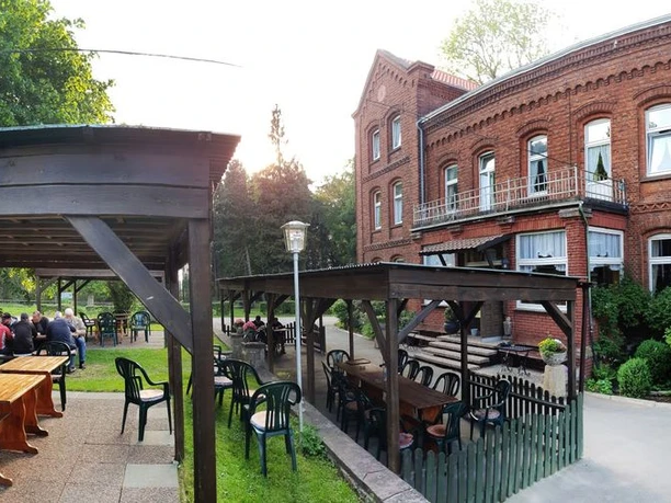 004-Gut-Externbrock-Aussenanlage_web.jpg Historische Backsteinfassade eines Gebäudes mit angrenzender überdachter Terrasse und Sitzmöglichkeiten.