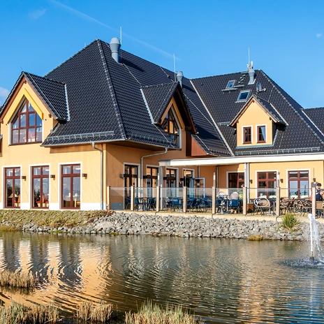Restauracja z tarasem, położona nad małym stawem, nowoczesna architektura, błękitne niebo.