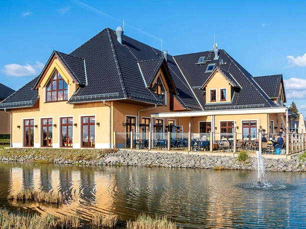 Restauracja z tarasem, położona nad małym stawem, nowoczesna architektura, błękitne niebo.