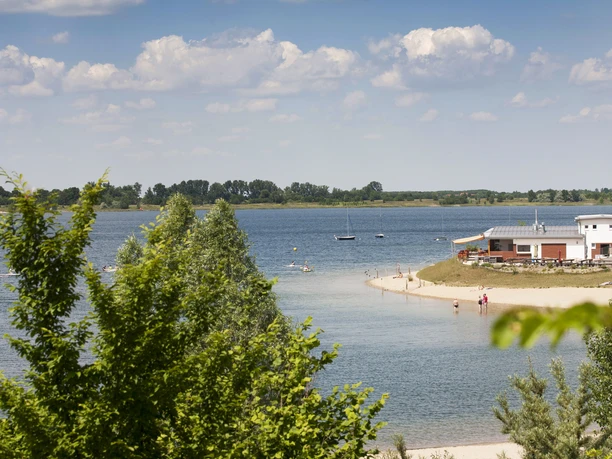 Plage de sable et baigneurs au lac de Schladitz avec une vue claire sur l'eau et le complexe sportif.