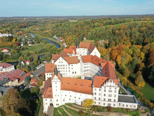 Vue aérienne du château de Colditz en automne avec le paysage environnant boisé et coloré.