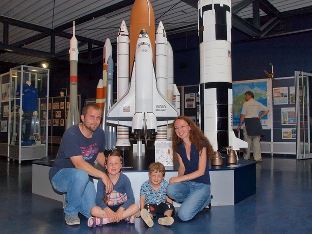 Family sits in front of a model of a space shuttle at the German Space Exhibition.