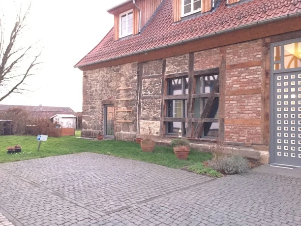 Ferienwohnung Historische Scheune - Außenansicht Historische Scheune mit Ziegeldach und Fachwerkfassade, umgeben von gepflastertem Hof und Grünfläche.