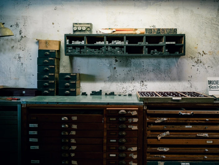 Graue Wand mit etlichen Regalen mit Schubladen davor, Werkstadttcharakter