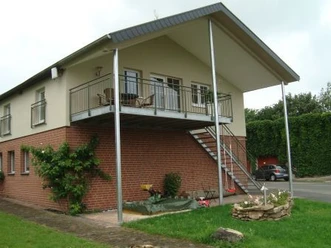 Ferienwohnung Böhlen Zweistöckiges Haus mit überdachtem Balkon, Ziegel- und Putzfassade, Außentreppe und Garten.