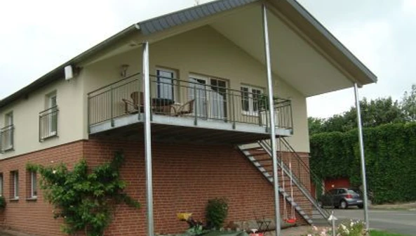 Ferienwohnung Böhlen Zweistöckiges Haus mit überdachtem Balkon, Ziegel- und Putzfassade, Außentreppe und Garten.