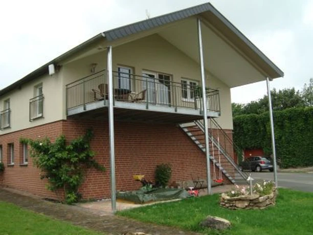Ferienwohnung Böhlen Zweistöckiges Haus mit überdachtem Balkon, Ziegel- und Putzfassade, Außentreppe und Garten.