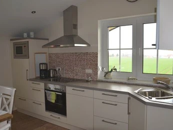 Ferienwohnung Böhlen - Küche Moderne Küche mit Edelstahlherd und -spüle, weißen Schränken und großem Fenster mit Feldblick.