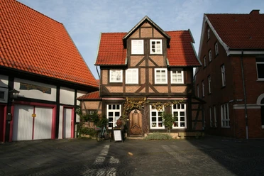 Ein traditionelles Fachwerkgebäude mit markantem roten Ziegeldach, begrüntem Eingang und dekorativem Türschild.