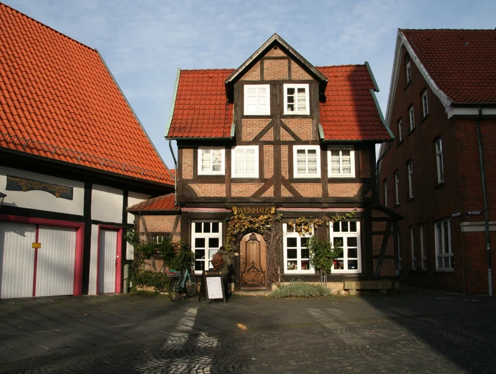 Ein traditionelles Fachwerkgebäude mit markantem roten Ziegeldach, begrüntem Eingang und dekorativem Türschild.