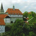 Ferienwohnung Am historischen Rathaus Historisches Fachwerkgebäude mit roten Ziegeldächern, umgeben von grünen Bäumen und einem Kirchturm.