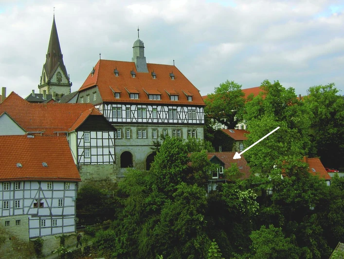 Ferienwohnung Am historischen Rathaus Historisches Fachwerkgebäude mit roten Ziegeldächern, umgeben von grünen Bäumen und einem Kirchturm.