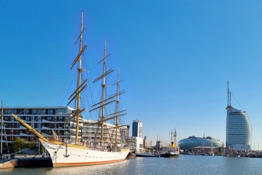 Segelschiff im Hafen von Bremerhaven vor modernen Gebäuden und dem markanten Sail City Hotel.