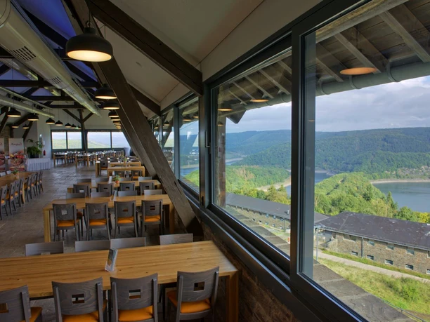 Gastronomie Vogelsang IP Innenraum eines Restaurants mit mehreren Tischgruppen vor einer Glasfront mit Aussicht auf einen See.