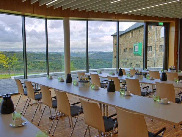 Panoramaraum Vogelsang IP Konferenzraum mit langen Tischen und einer Glasfront mit Blick auf hügelige Landschaft.