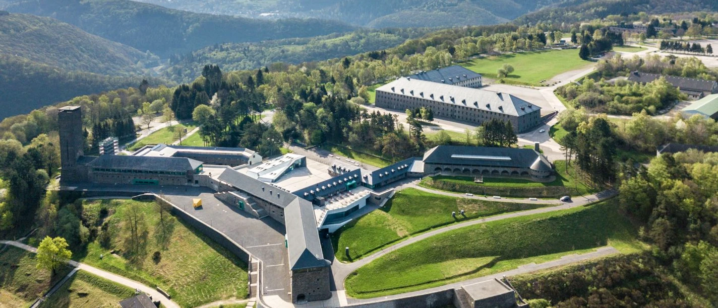Festungsähnliches Gelände inmitten einer hügeligen Landschaft mit symmetrisch angeordneten Gebäuden und gepflegten Grünflächen.