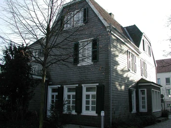 Ein traditionelles, graues Schieferhaus mit weißen Fensterrahmen steht an einem winterlichen Tag.