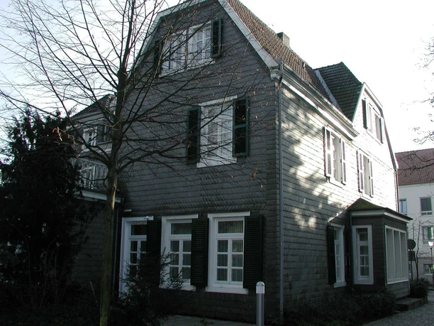 Kirchstraße Traueingang Ein traditionelles, graues Schieferhaus mit weißen Fensterrahmen steht an einem winterlichen Tag.