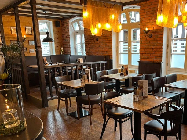 NieheimRestaurantDakos.jpg Restaurant mit dunklen Holzmöbeln, warmen Beleuchtung und Backsteinwänden, einladender Innenraum.