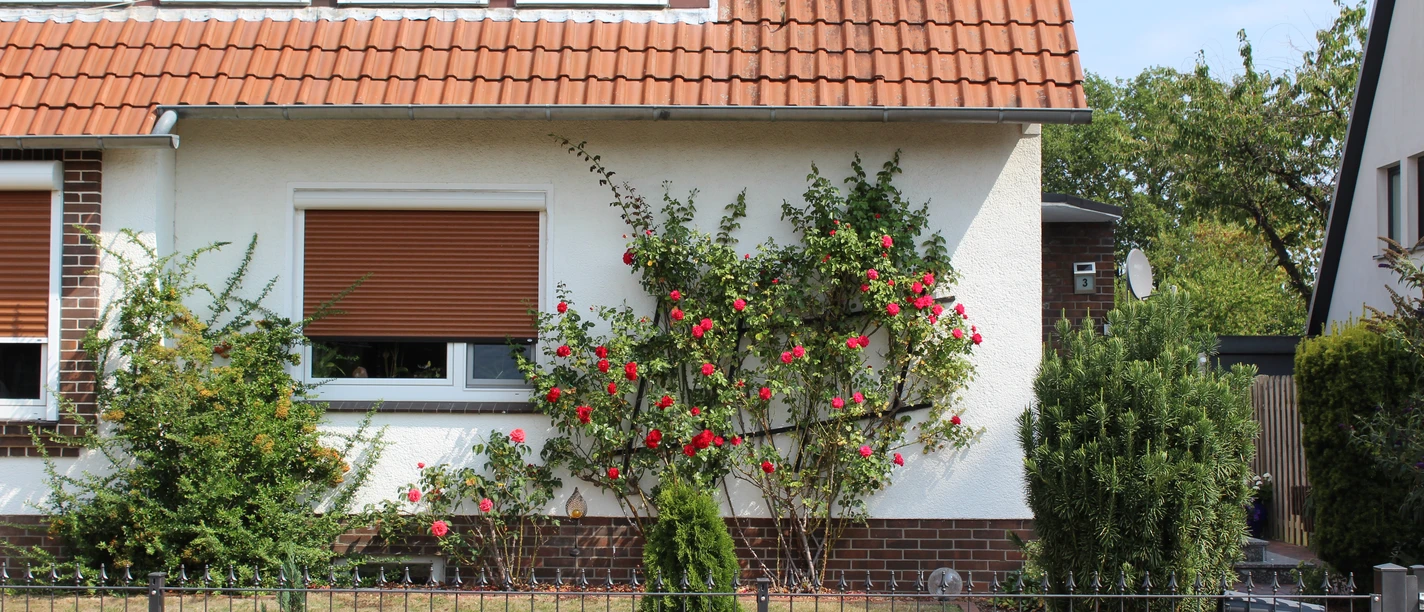 FeWo Pohlmann Ferienwohnung in einem Haus mit roten Dachziegeln, umgeben von gepflegtem Garten und Rosenstrauch.