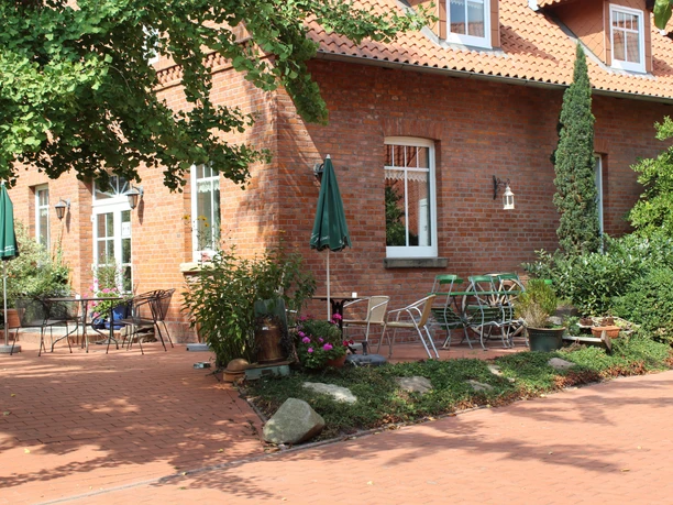 Red brick building with terrace, garden furniture and green plants under blue parasols.