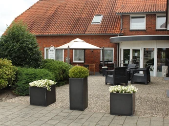 Eingangsbereich eines traditionellen Backsteinhauses mit roten Dachziegeln und gepflegten Pflanzen.